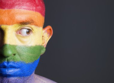 Gay flag painted on the face of a man. Man is looking sideways clipart