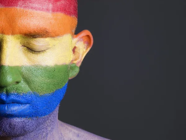 Schwulenflagge auf das Gesicht eines Mannes mit geschlossenen Augen gemalt. — Stockfoto