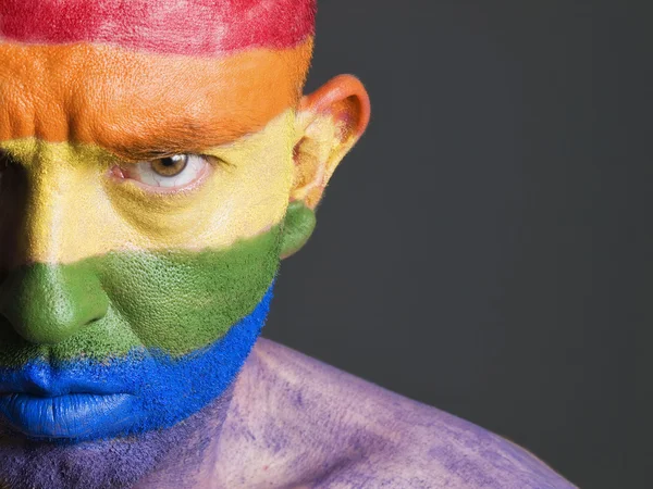 Schwulenfahne auf das Gesicht eines Mannes gemalt, ernster Ausdruck. — Stockfoto