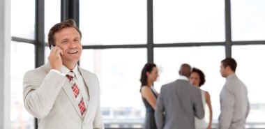 Smiling businessman holding a phone at workplace with his collea clipart