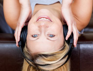 Delighted woman lies on a sofa and listen music clipart