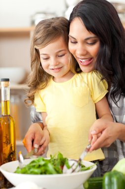 Brunette mother helping her daughter prepare salad clipart