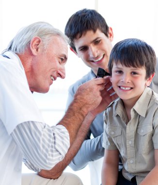 Senior doctor examining a little boy's ears clipart