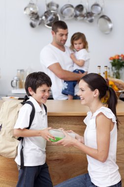 Smiling mother giving school lunch to her son clipart