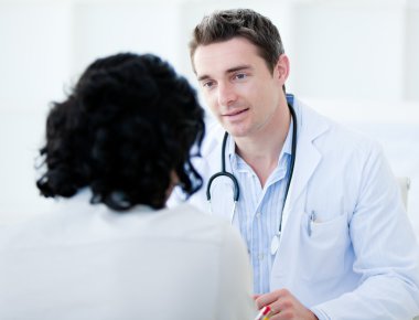 Handsome doctor talking with his patient for the annual check-up clipart