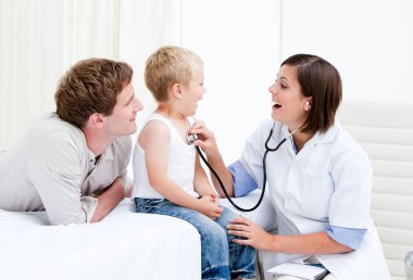 Radiant female doctor examining a little boy with his father clipart