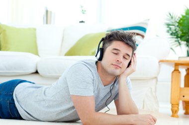 Charming young man listen to music lying on the floor clipart