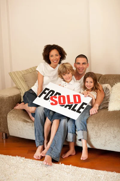 Giovane famiglia seduta sul divano con una plakat — Foto Stock
