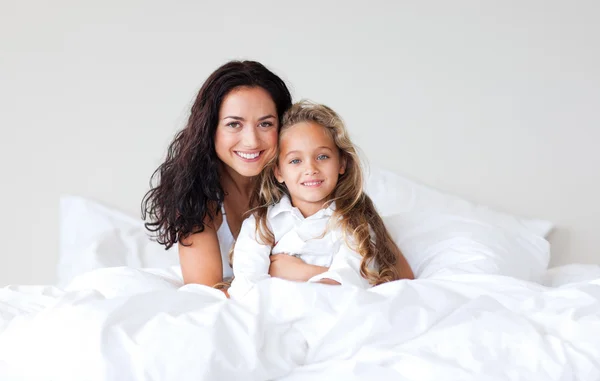 Brunett mamma och hennes leende dotter på sängen — Stockfoto