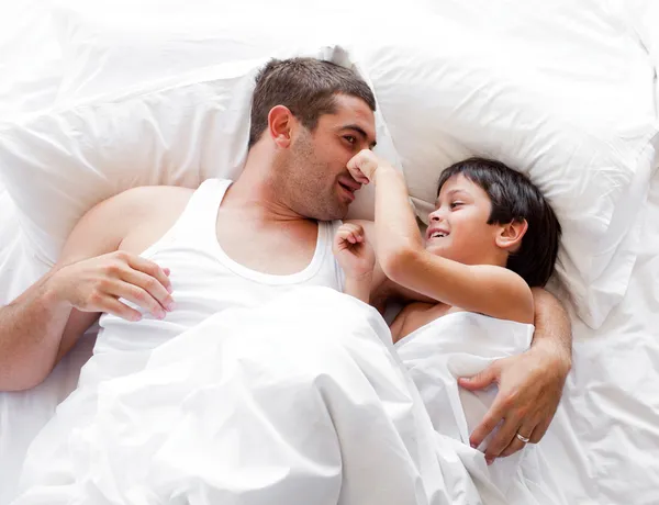 Usmívající se dítě hraje s jeho otcem, ležící na posteli doma — Stock fotografie
