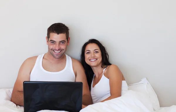 Lyckliga paret använder en bärbar dator som ler mot kameran — Stockfoto