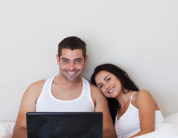 Encantado casal sentado na cama com laptop — Fotografia de Stock