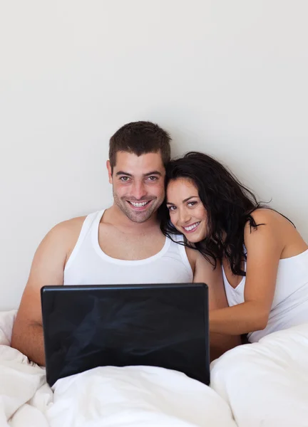 Gülümseyen çift yatakta yatan bir dizüstü bilgisayar kullanarak — Stok fotoğraf
