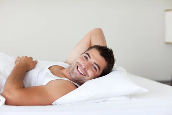Hombre atractivo en una cama sonriendo a la cámara — Foto de Stock