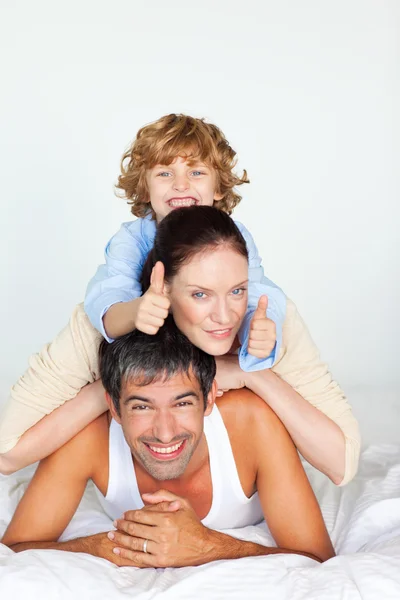 Family having fun in bed with thumbs up — Stock Photo, Image