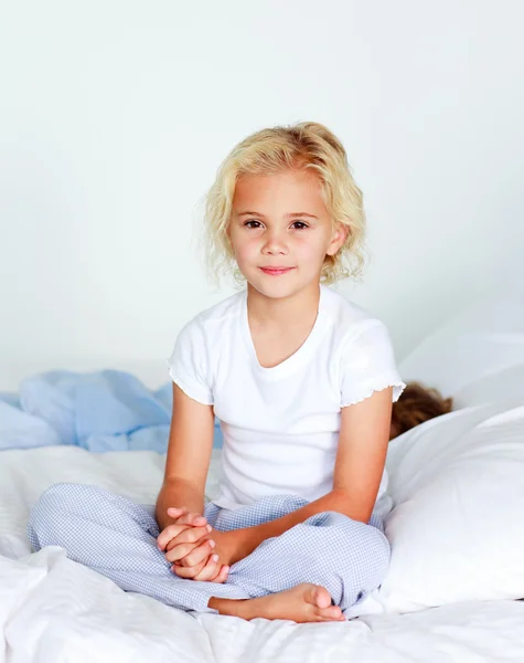 Carino piccola ragazza bionda seduta sul suo letto — Foto Stock
