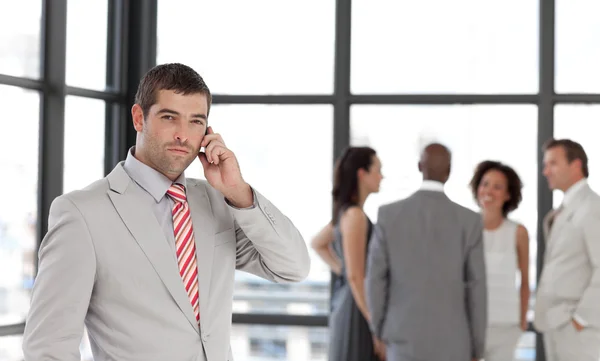 Self-assured businessman holding a phone at workplace with his c — Stock Photo, Image