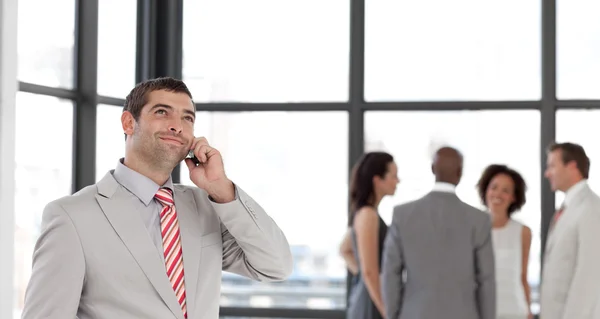 Uomo d'affari che tiene un telefono sul posto di lavoro con i suoi colleghi — Foto Stock