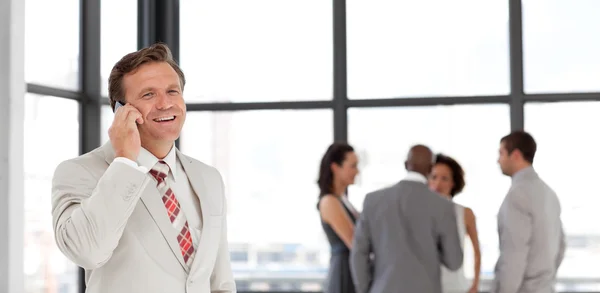 Smiling businessman holding a phone at workplace with his collea — Stock Photo, Image