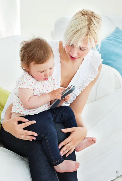 Mulher loira usando um controle remoto com sua menina na sala de estar — Fotografia de Stock