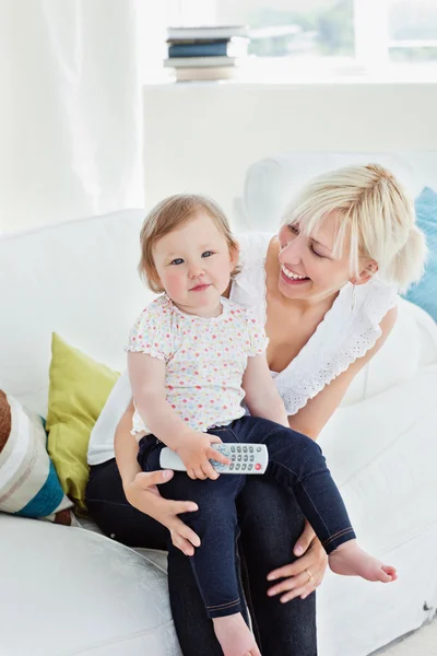 Young woman using a remote with her girl in the living-room — Stock Photo, Image