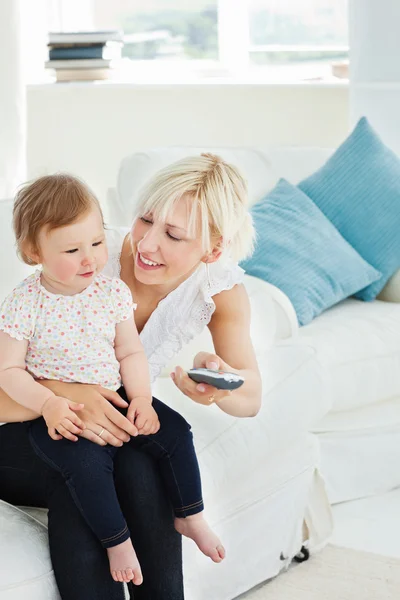 Mulher alegre usando um controle remoto com sua menina na sala de estar — Fotografia de Stock