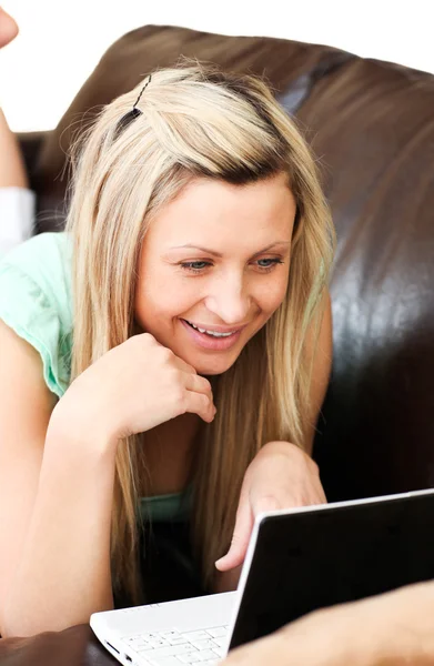 Mujer sonriente se encuentra en el sofá y trabaja en el ordenador portátil —  Fotos de Stock