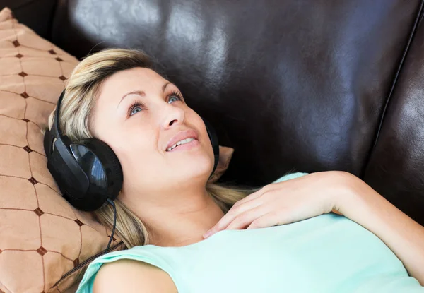 Young woman lies on a sofa and listen music — Stock Photo, Image