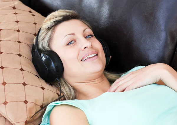 Donna sorridente si trova su un divano e ascoltare musica — Foto Stock