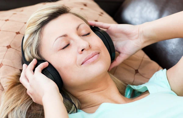 Mulher relaxada deita-se em um sofá e ouvir música — Fotografia de Stock
