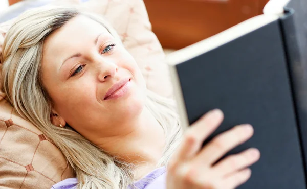 Сяюча жінка лежить на дивані і читає книгу — стокове фото