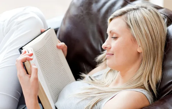Γοητευτική γυναίκα διαβάζοντας ένα βιβλίο καθμένος σε έναν καναπέ — Φωτογραφία Αρχείου