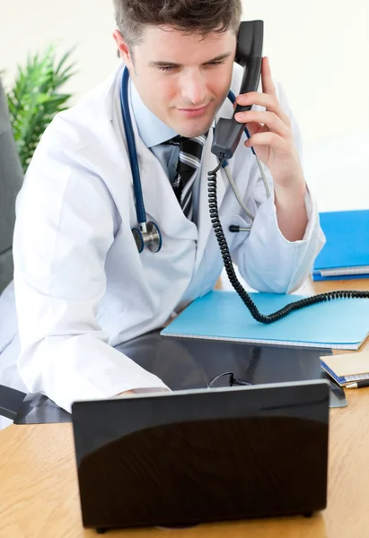 Médico masculino positivo en el teléfono usando su computadora portátil —  Fotos de Stock