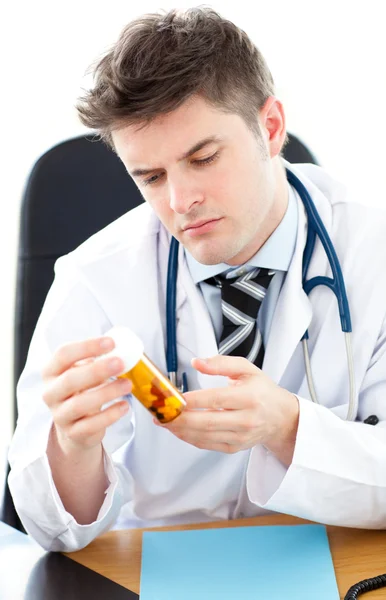 Médico masculino serio sosteniendo pastillas sentado en su escritorio —  Fotos de Stock