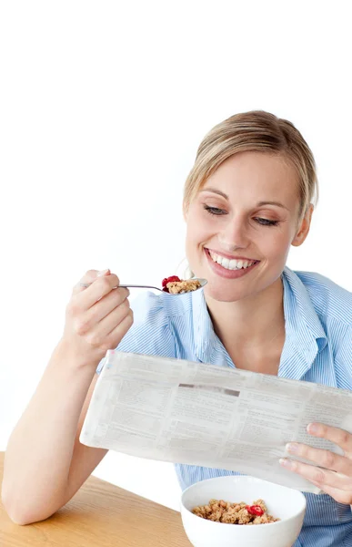 Glowing woman eating cereals while reading newspaper — Stock Photo, Image