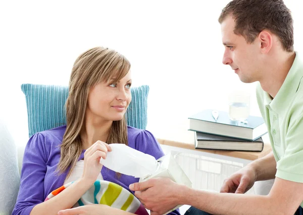 Caring man giving his ill girlfriend tissue lying on a sofa — Stock Photo, Image