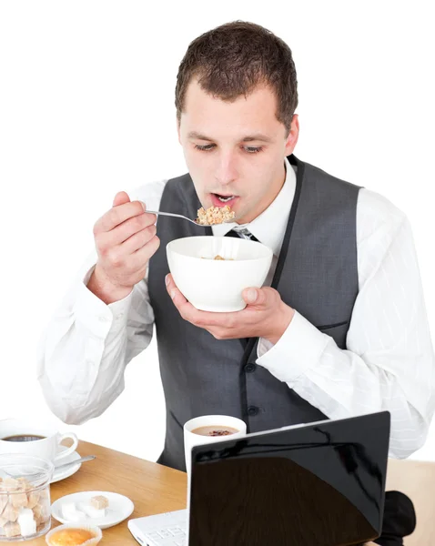 Concentrated businessman eating cereals looking at his laptop — Stock Photo, Image
