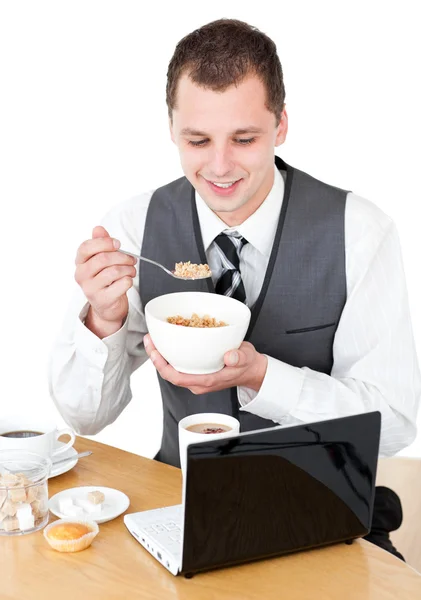 Homem de negócios feliz comendo cereais olhando para seu laptop — Fotografia de Stock