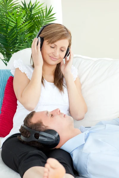 Mujer linda escuchando música con su novio acostado en un sofá —  Fotos de Stock