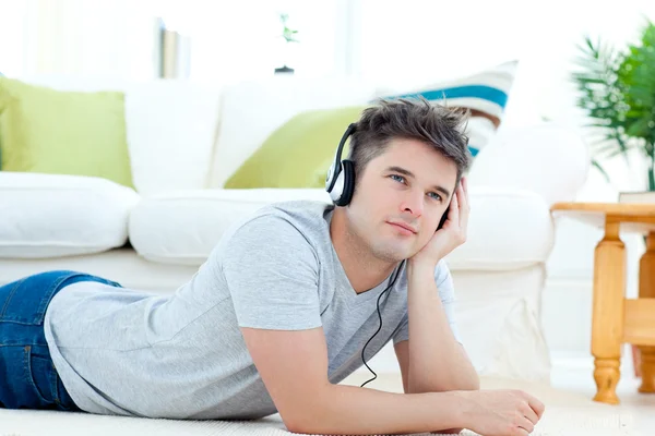 Mladý muž se sluchátky, které leží na podlaze v obývacím pokoji — Stock fotografie