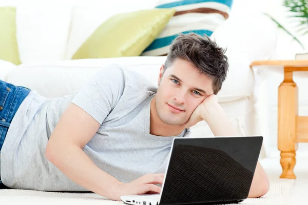 Przystojny młody mężczyzna leży na podłodze z laptopa — Zdjęcie stockowe