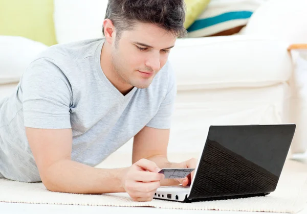 Hombre concentrado sosteniendo una tarjeta de crédito mirando un portátil —  Fotos de Stock