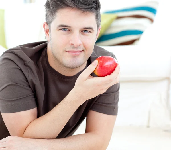 Веселий чоловік тримає червоне яблуко, що лежить на підлозі — стокове фото