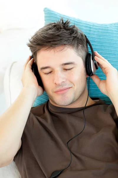 Atrakcyjny młody człowiek, słuchanie muzyki, leżąc na kanapie — Zdjęcie stockowe