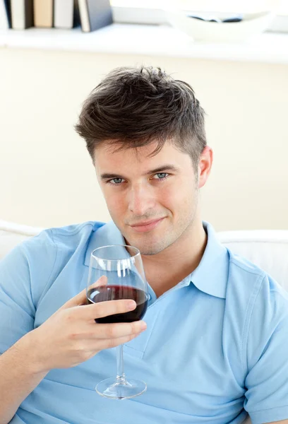 Bello giovane seduto su un divano con in mano un bicchiere da vino — Foto Stock