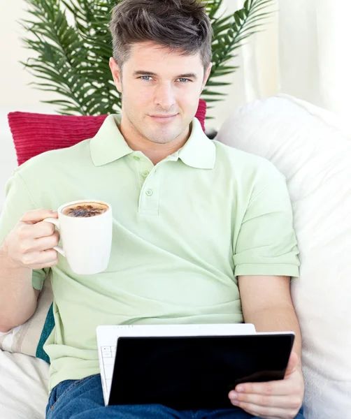 Joyful young man holding a cup of coffee and a laptop — Stock Photo, Image