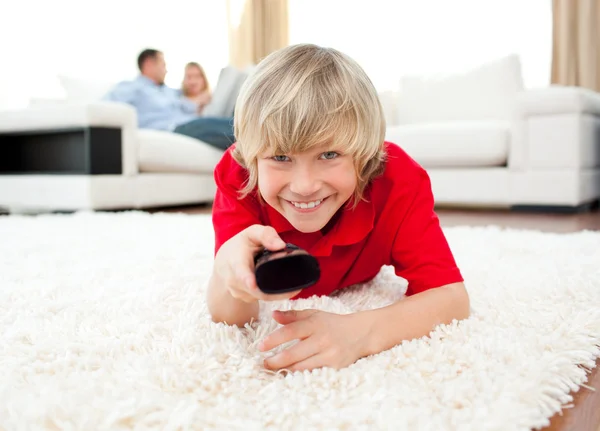 Happy boy holding a remote lying on the floor — Stock Photo, Image
