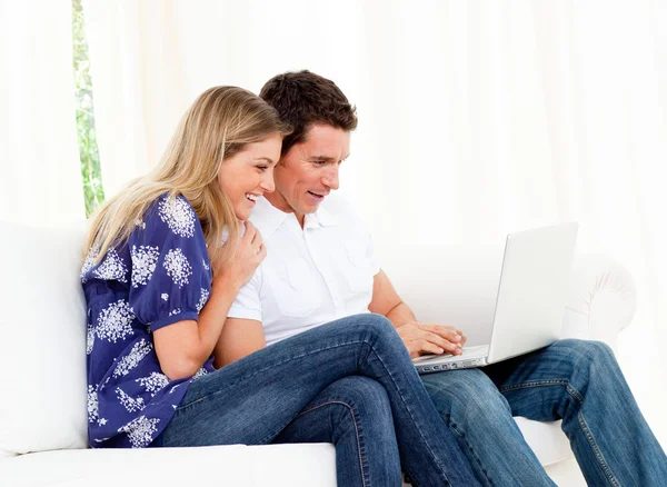 Casal animado usando um laptop sentado no sofá — Fotografia de Stock