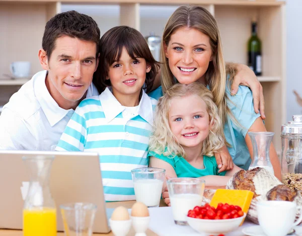Familia alegre usando el ordenador portátil durante el desayuno —  Fotos de Stock