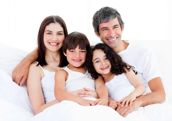 Porträtt av en lycklig familj sitter på en säng — Stockfoto